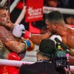 Intense boxing match between Jake Paul and Anthony Joshua with fighters exchanging punches in the ring.