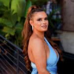 Joy Taylor in a blue dress, standing outdoors with greenery in the background, related to the Joy Taylor lawsuit case.