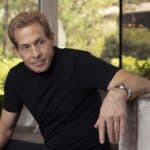 Image of Skip Bayless, sports commentator, sitting on a sofa in a modern living room, discussing legal issues related to his lawsuit.