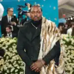 Stefon Diggs at a public event, dressed in a black suit with a fur stole, surrounded by media and fans, highlighting his legal situation regarding paternity allegations.