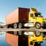 Yellow semi-truck parked near water with industrial cranes in the background, highlighting legal issues related to CDL cancellations in California.