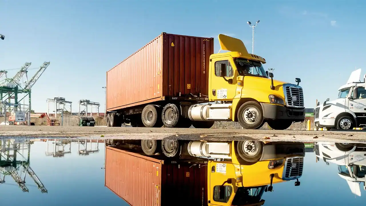 Yellow semi-truck parked near water with industrial cranes in the background, highlighting legal issues related to CDL cancellations in California.
